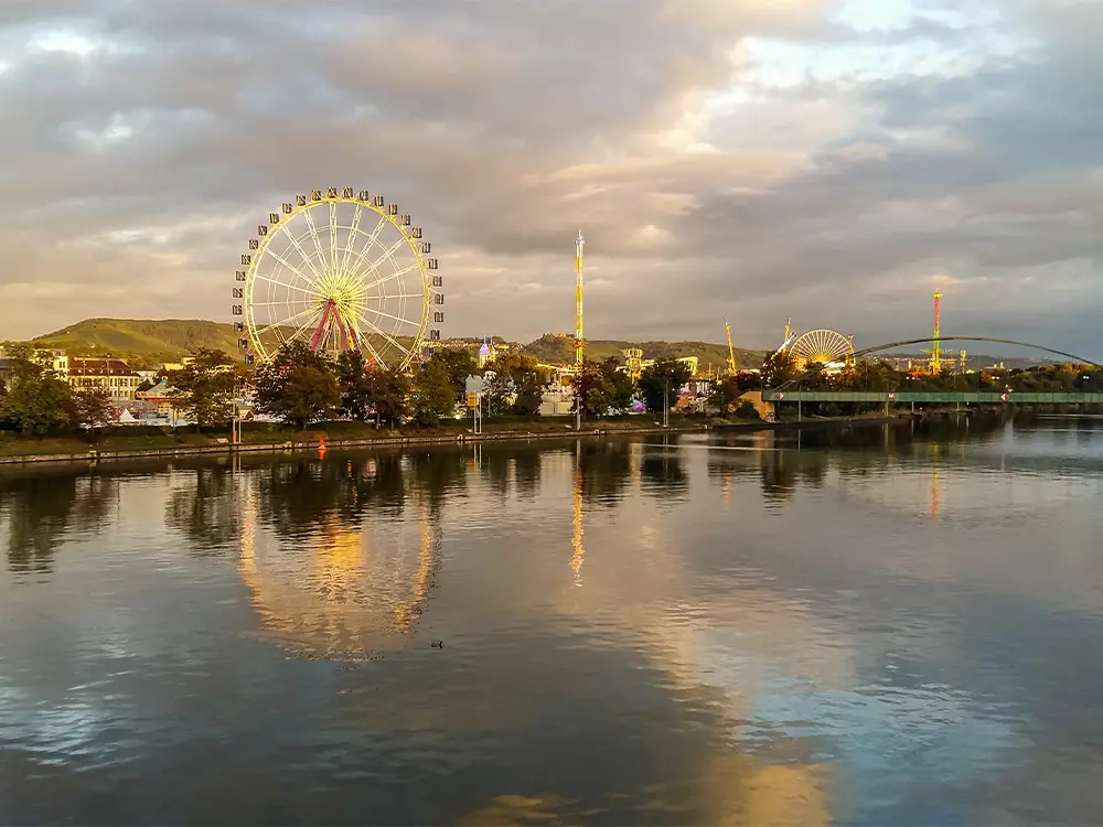 Ferris wheel and fairgrounds at the Cannstatter Volksfest reflected in the Neckar River at sunset.