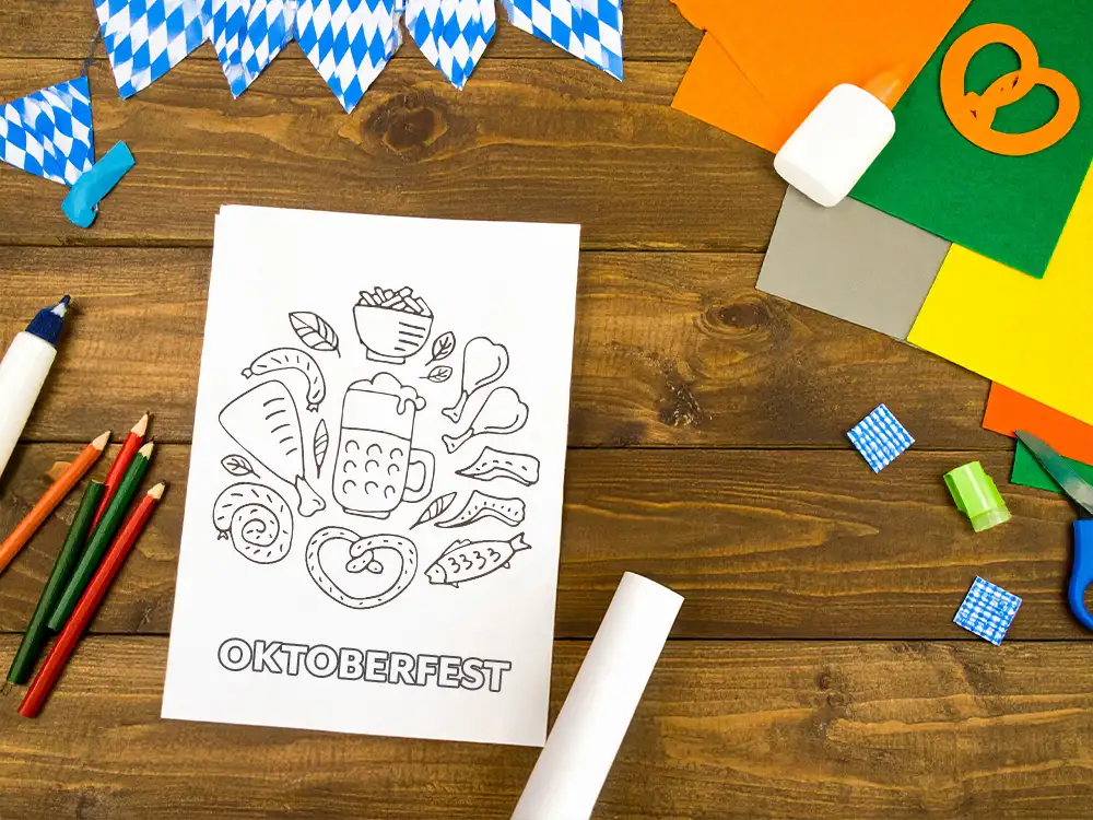 Children’s Oktoberfest-themed coloring page on a wooden table surrounded by craft supplies and Bavarian decorations.