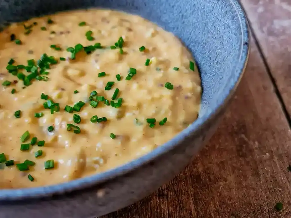 Close-up of creamy Obatzda cheese dip garnished with chopped chives in a rustic ceramic bowl.