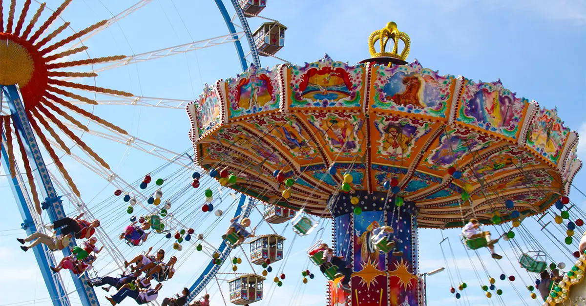 Colorful spinning swing ride and Ferris wheel at a German Oktoberfest fairground on a sunny day.
