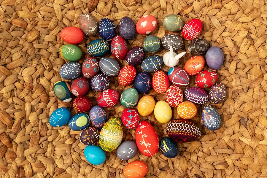 A variety of colorful, decorated eggs arranged on a woven mat.