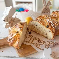 Sliced Hefezopf German Easter bread with raisins, pearl sugar and almond flakes on a wooden board, surrounded by Easter eggs and decorations
