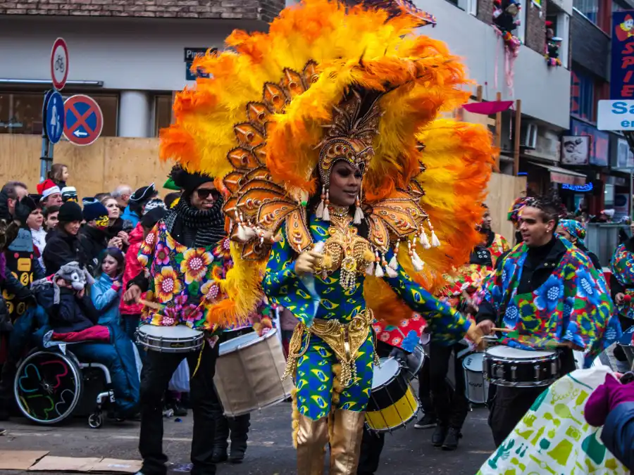 Cologne Karneval dancer in an orange feather headdress and gold costume, with drummers behind in Köln
