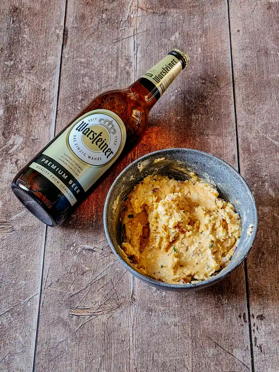 Obatzda before the beer. Bavarian-style Obatzda beer cheese dip served in a bowl with a Warsteiner beer bottle in the background.
