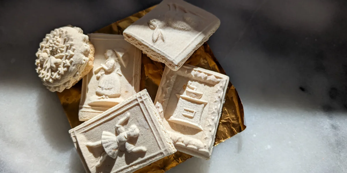 Traditional German Springerle cookies with embossed designs, dusted with flour and stacked on gold foil.