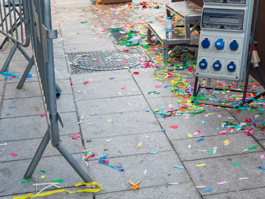 Confetti and streamers scattered on a city sidewalk after Karneval, the messy handoff to Lent in Germany.