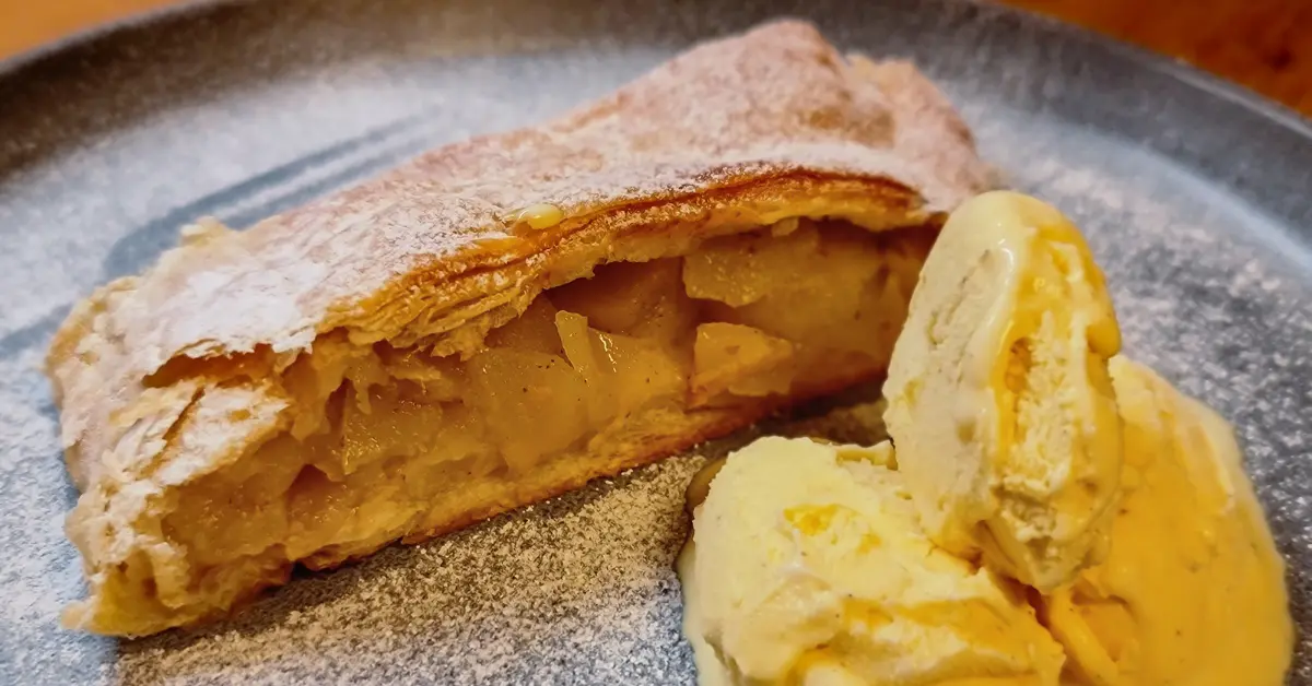 Golden pastry filled with apples on a grey plate with ice cream.