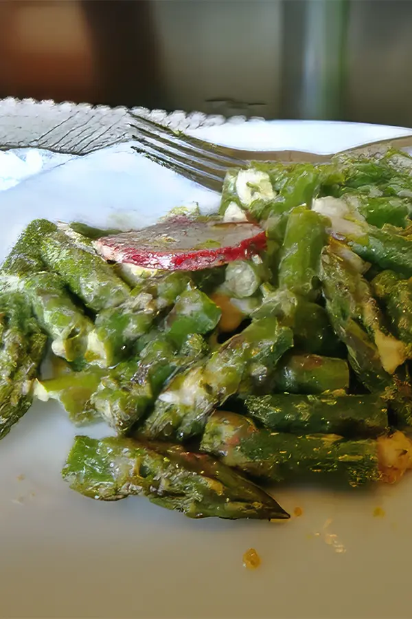 A plate of green asparagus in creamy sauce, garnished with sliced radish, with a fork on the side.