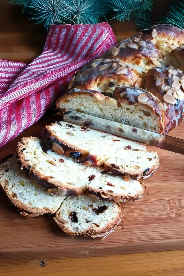 Sliced braided bread on a wooden board, beside a red and white striped cloth.