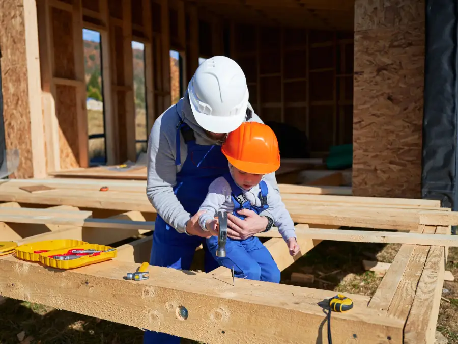 Adult guiding a child with a hammer at a house construction site, nod to German innovators in history