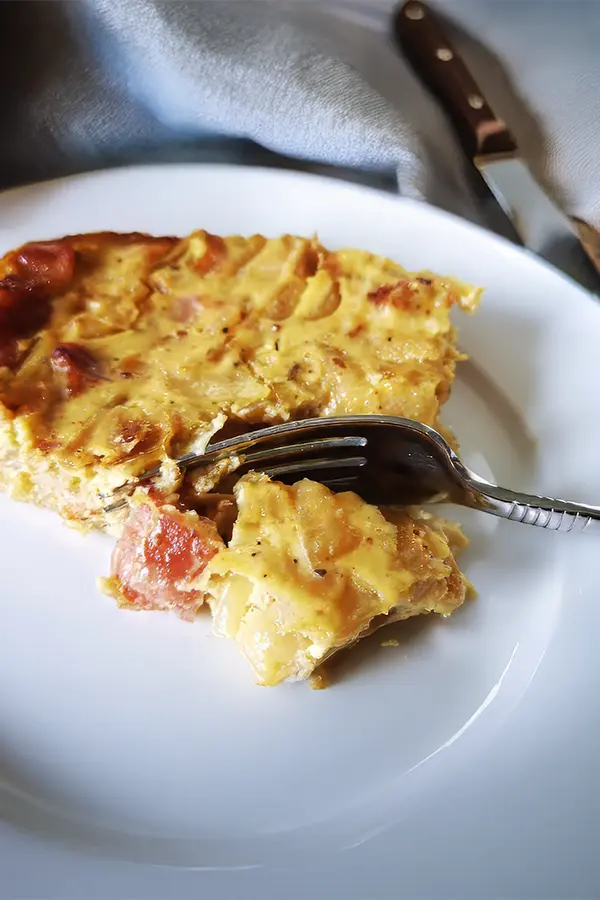 A slice of onion tart with visible chunks of meat on a white plate, partially eaten, with a fork resting on top.