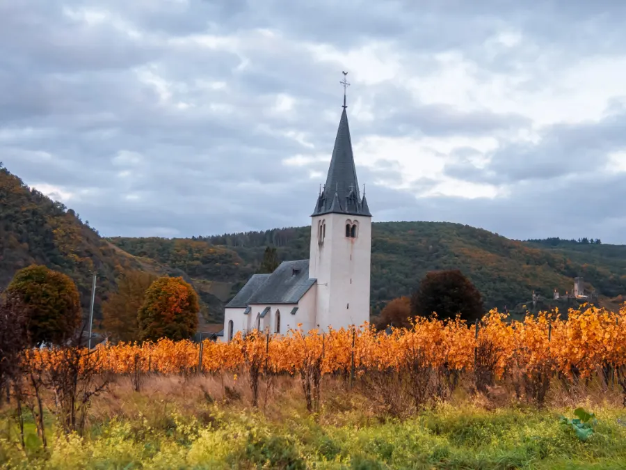Small white church with tall steeple overlooking autumn vineyards and hills, a quiet regional Lent tradition setting.