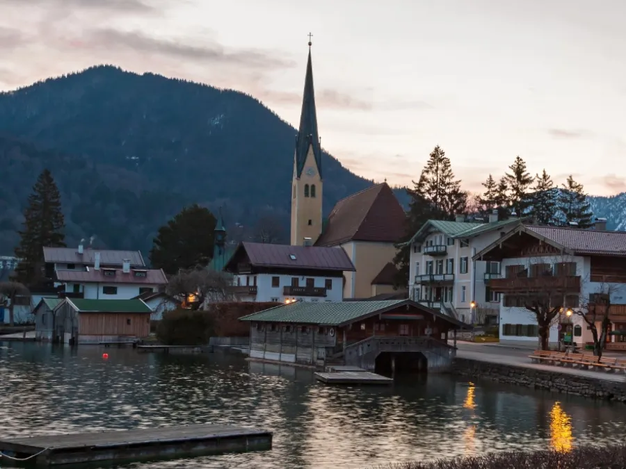 Lakeside village with church steeple and mountains at dusk, the calm early-spring vibe of Fastenzeit.