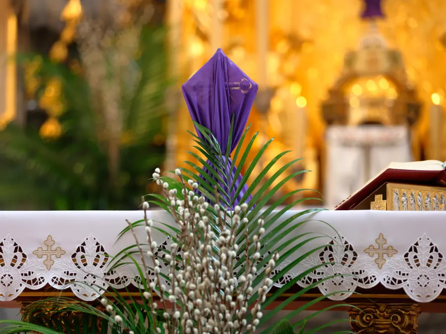 Purple-veiled cross on a church altar with palm fronds and willow branches, Lent church decor in Germany.