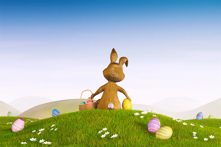 Easter Bunny on a hill. A brown rabbit sits on grassy hill with Easter eggs, holding a yellow egg. Basket of eggs beside it. Clear blue sky in background.