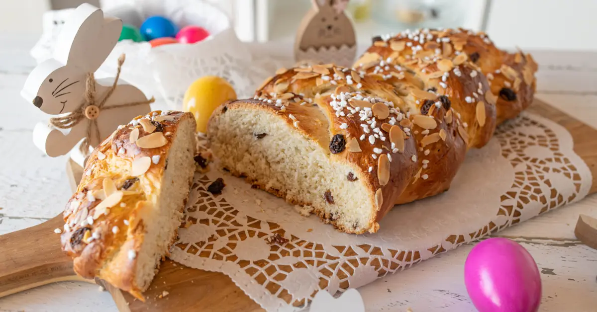 Sliced Hefezopf German Easter bread with raisins, pearl sugar and almond flakes on a wooden board, surrounded by Easter eggs and decorations
