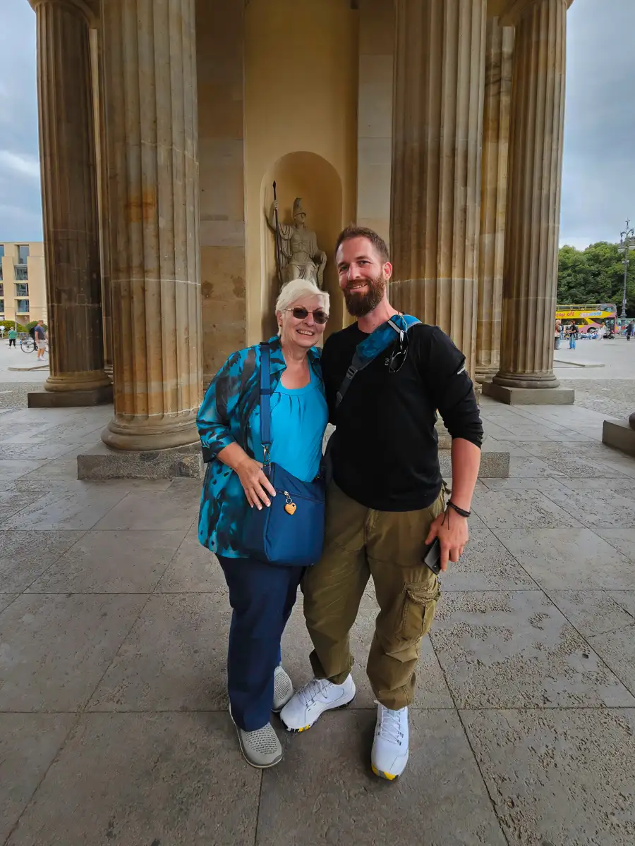 Smiling son and mother pose together in front of large neoclassical columns at Berlin’s Brandenburg Gate.