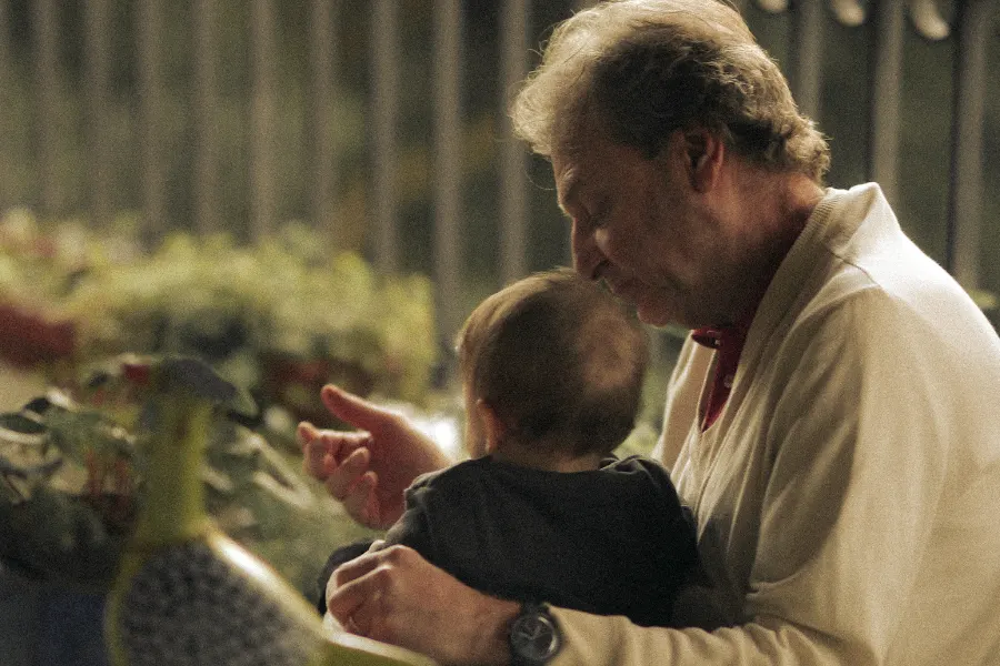 A grandfather holding an infant grandchild, the unannounced moment where most cultural transmission actually happens.