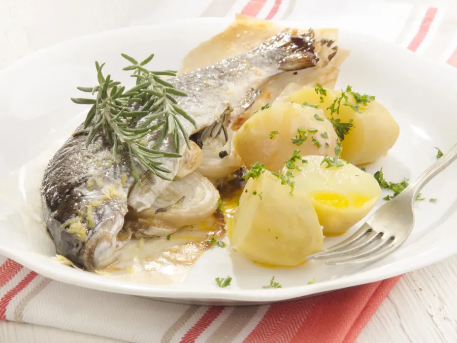 Cooked fish with boiled potatoes, rosemary, and herbs on a white plate, simple Fastenzeit food in Germany.