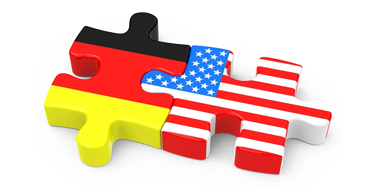 Two interlocked puzzle pieces featuring the flags of Germany and the United States, symbolizing cultural connection or international cooperation, on a white background.