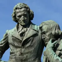 Close-up of the monument to Jacob and Wilhelm Grimm, featuring the two brothers in thoughtful poses against a clear blue sky.