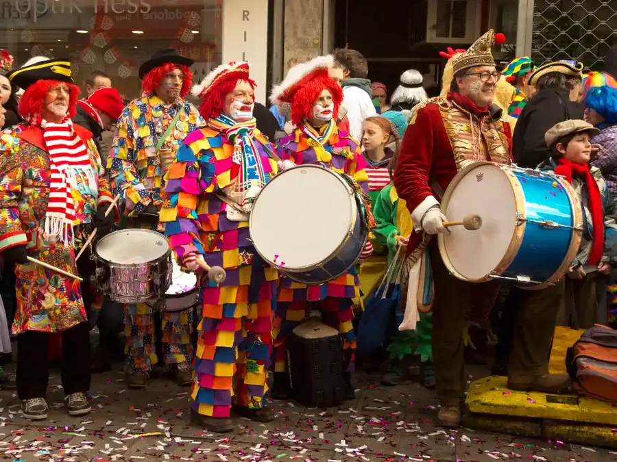 Colorful Karneval drummers in clown costumes on a crowded street, confetti covering the ground