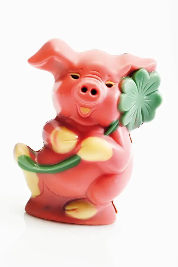 A pink ceramic pig figurine holding a green four-leaf clover.