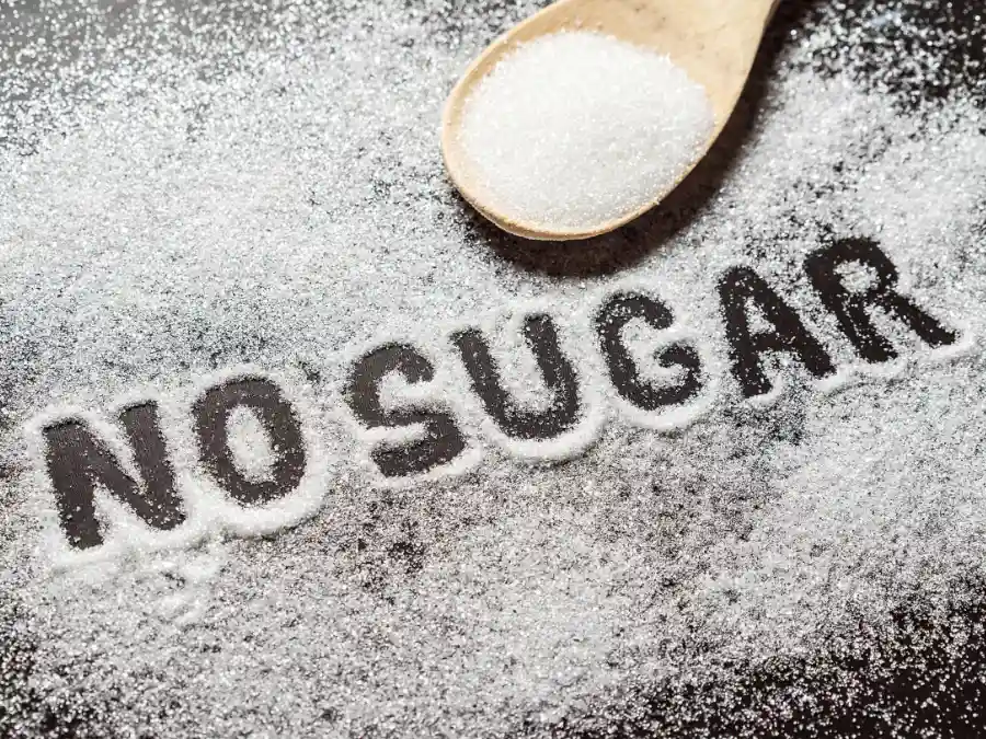 Granulated sugar spilled on a dark surface with “NO SUGAR” spelled out, a modern Fastenzeit vow in Germany.