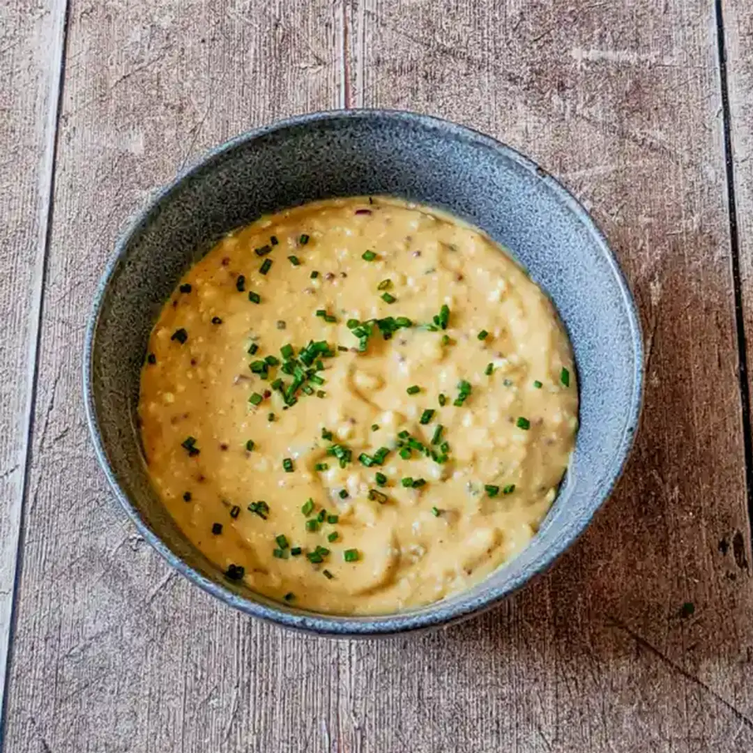 A bowl of Bavarian Obatzda cheese spread garnished with chopped chives, served on a rustic wooden surface.