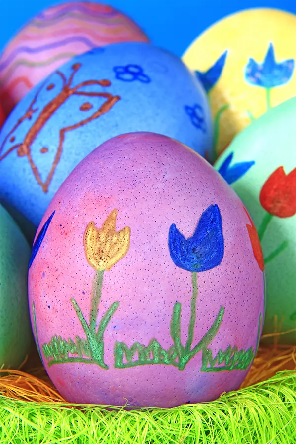 Colorful decorated Easter eggs with floral and butterfly designs, placed on vibrant green grass.