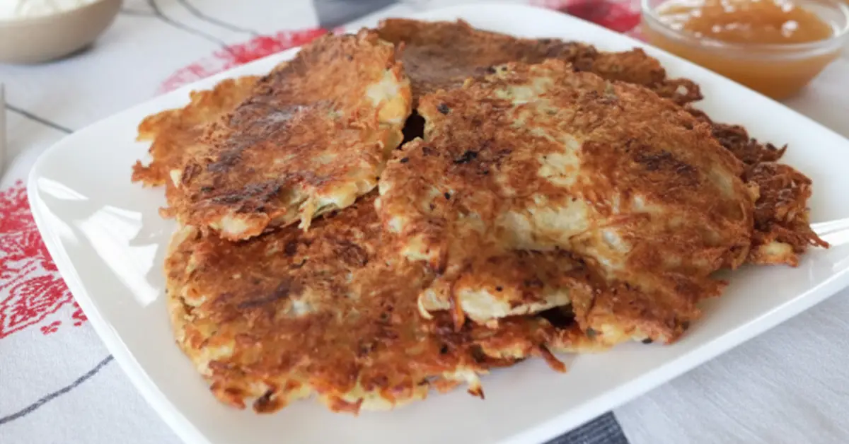 Traditional German potato pancakes (Reibekuchen or Kartoffelpuffer) served golden brown on a white plate, with applesauce on the side.