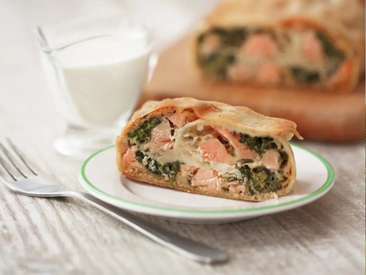 Slice of strudel with fish and spinach on a white plate.