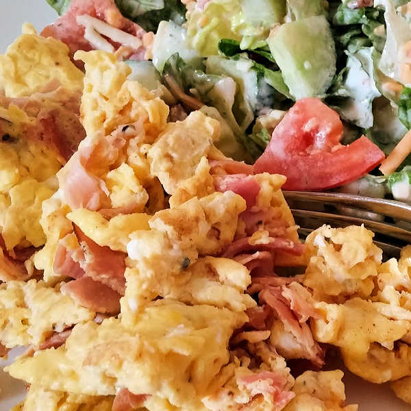 a plate of scrambled eggs and ham beside a salad