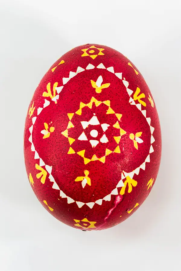 Red egg decorated with intricate yellow and white geometric and floral patterns, set against a plain white background.
