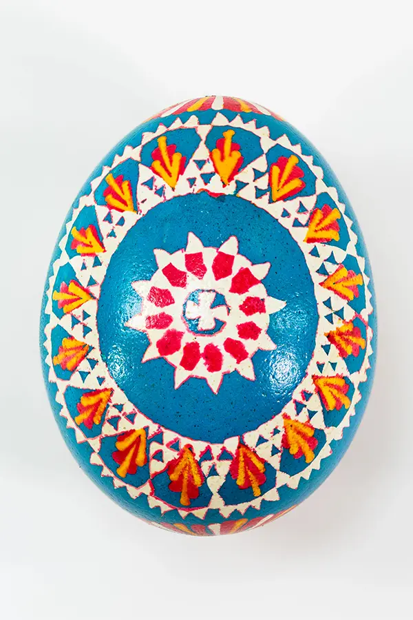 A blue egg with intricate red, yellow, and white geometric patterns and floral designs.