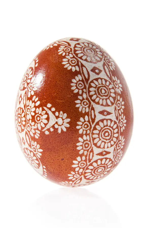 Ornate brown egg with intricate white floral and geometric patterns covering its surface.