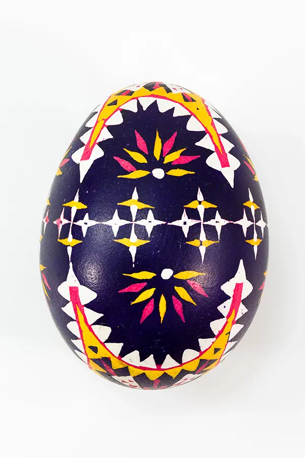 A decorative egg with a dark blue background, featuring intricate patterns in yellow, white, and pink.