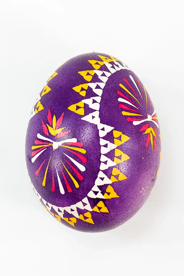 Purple egg decorated with colorful geometric patterns and fireworks-like designs in yellow, red, and white.