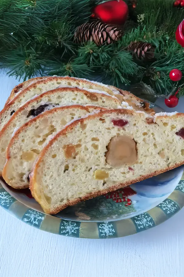 Slices of fruit-filled stollen on a festive plate, with a holiday-themed decoration of pine branches and red ornaments in the background.