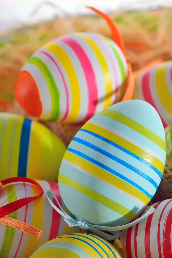A collection of colorful Easter eggs with various striped patterns, placed on a straw base.