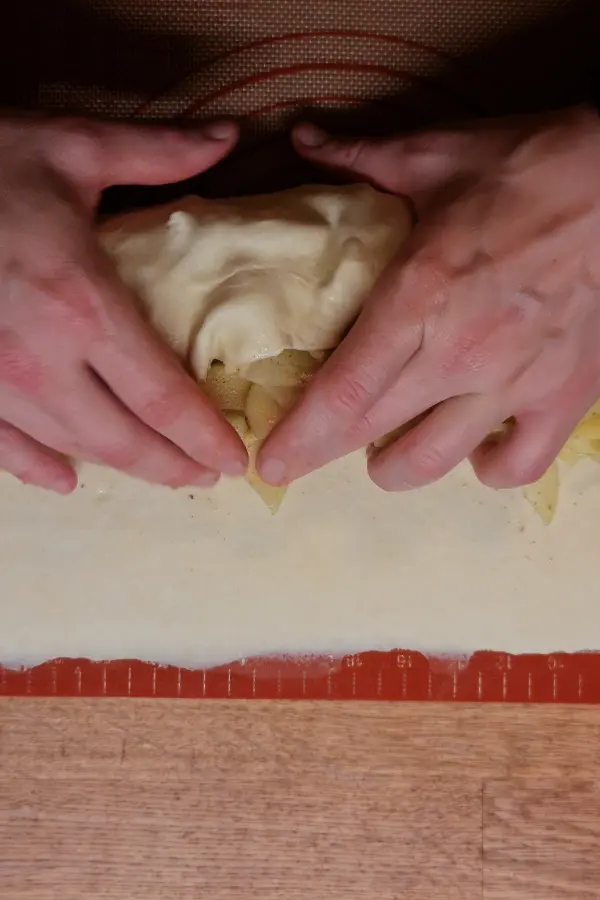 Two hands rolling up an apple strudel.