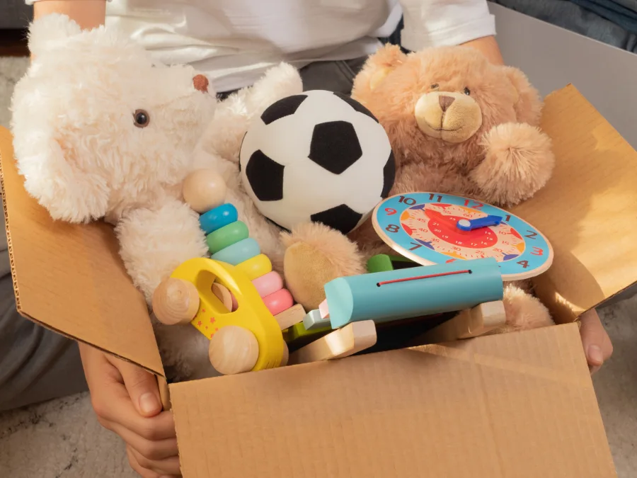 Hands holding a cardboard box of kids’ toys and teddy bears, a Lent practice of decluttering or donating during Fastenzeit.