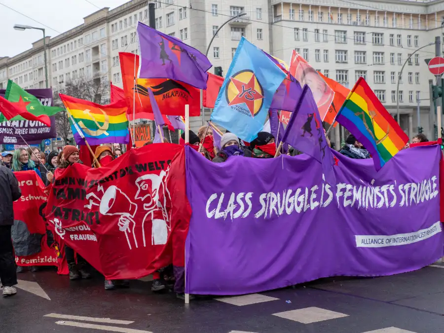 International Women’s Day march in Berlin with a purple banner, rainbow flags, and protesters on a city street.