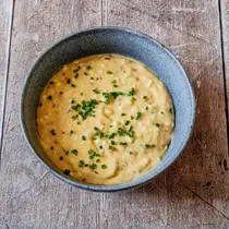 Top-down view of a rustic ceramic bowl filled with creamy Obatzda, a traditional Bavarian cheese spread, garnished with finely chopped chives and set on a weathered wooden surface.