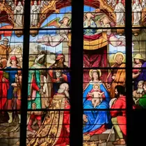 Detailed stained glass artwork depicting the Three Wise Men presenting gifts to the infant Jesus, with vibrant biblical figures and ornate designs.