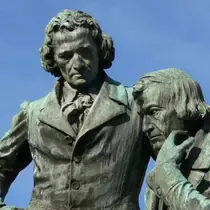 Close-up of the monument to Jacob and Wilhelm Grimm, featuring the two brothers in thoughtful poses against a clear blue sky.