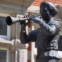 Bronze statue of the Pied Piper playing his pipe, located in Hamelin, Germany, in front of a historic building facade.