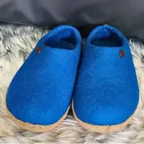 A pair of handmade blue wool slippers with cork soles resting on a soft, furry rug, reflecting traditional German craftsmanship.